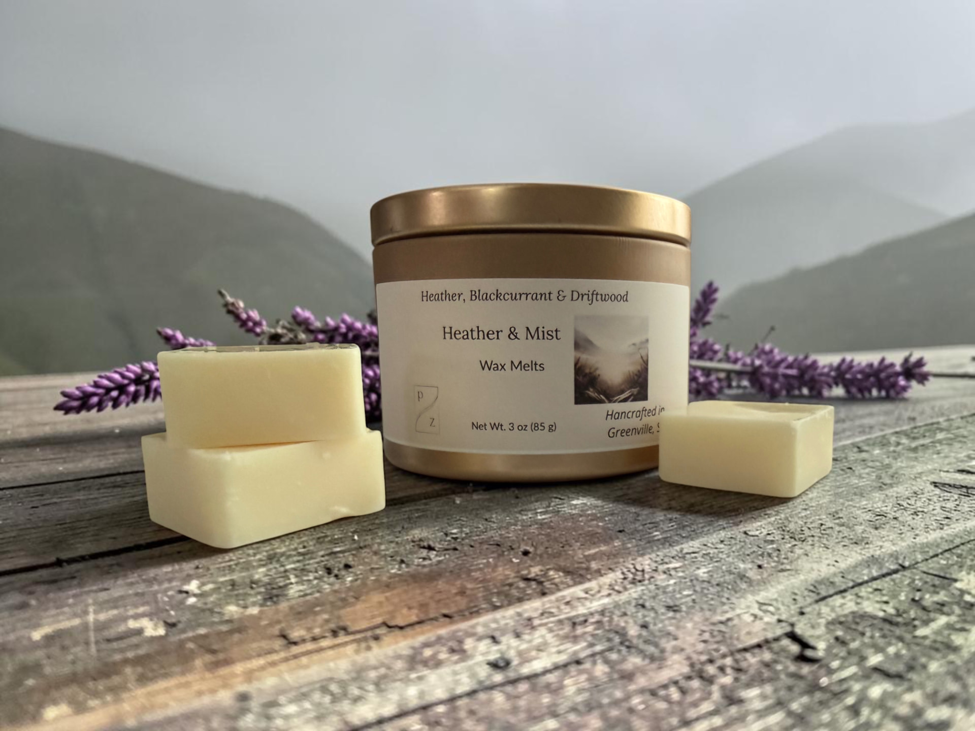 Heather & Mist Wax Melts, a gold tin with creamy wax melt squares on weathered wood with purple heather and misty hills