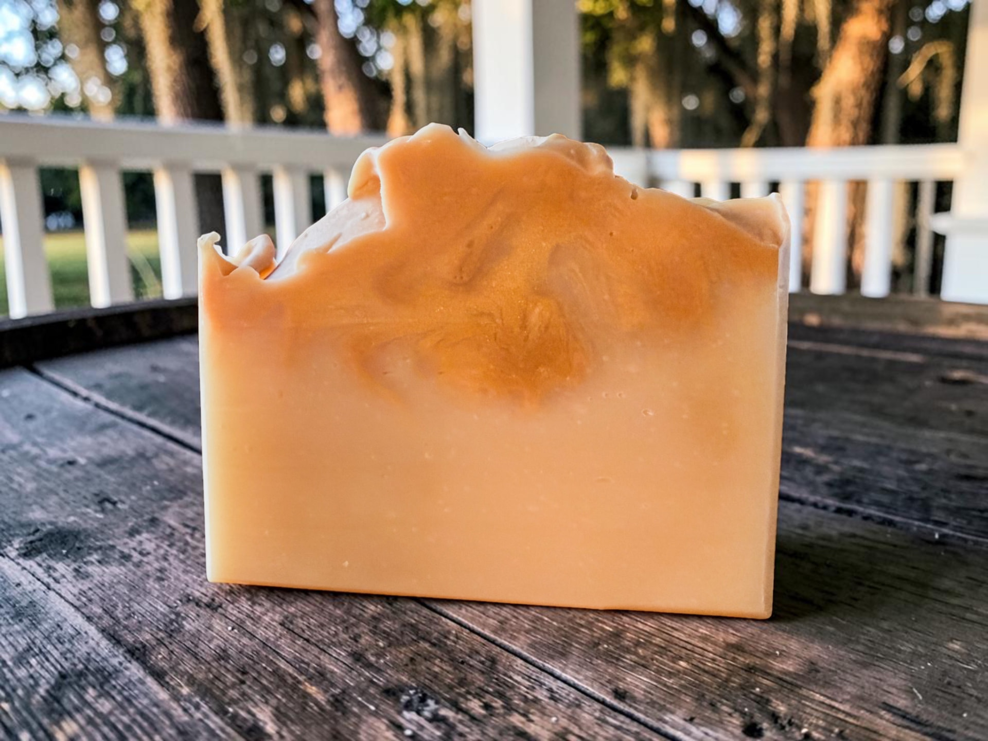 Lowcountry Muse Soap, a pale golden handmade bar with a swirled, shimmery top resting on weathered wood outdoors