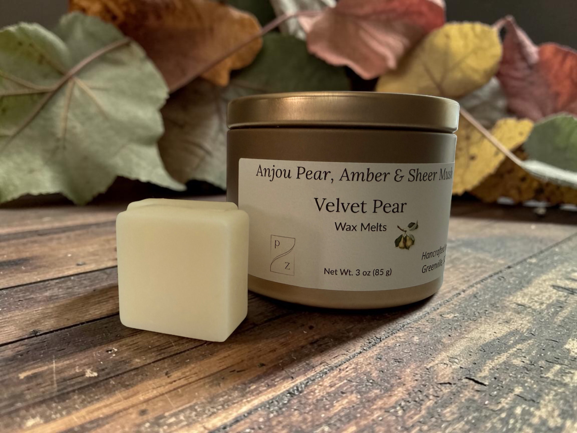 Velvet Pear Wax Melts, a gold tin with creamy wax melt squares beside a single melt on weathered wood with autumn leaves