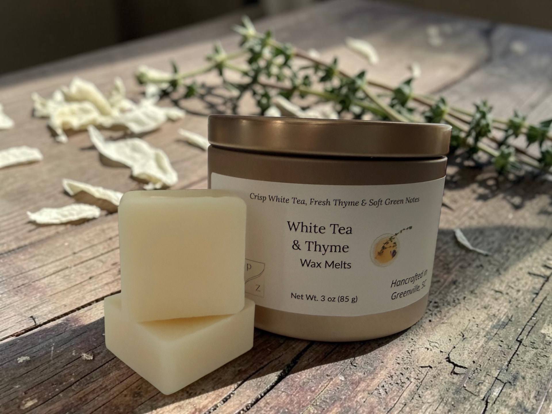 White Tea & Thyme Wax Melts, a gold tin with creamy wax melt squares on weathered wood with fresh thyme and white tea leaves